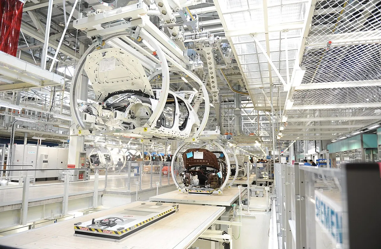 Vehicle bodies in rotating assembly carriers inside a bright production hall.