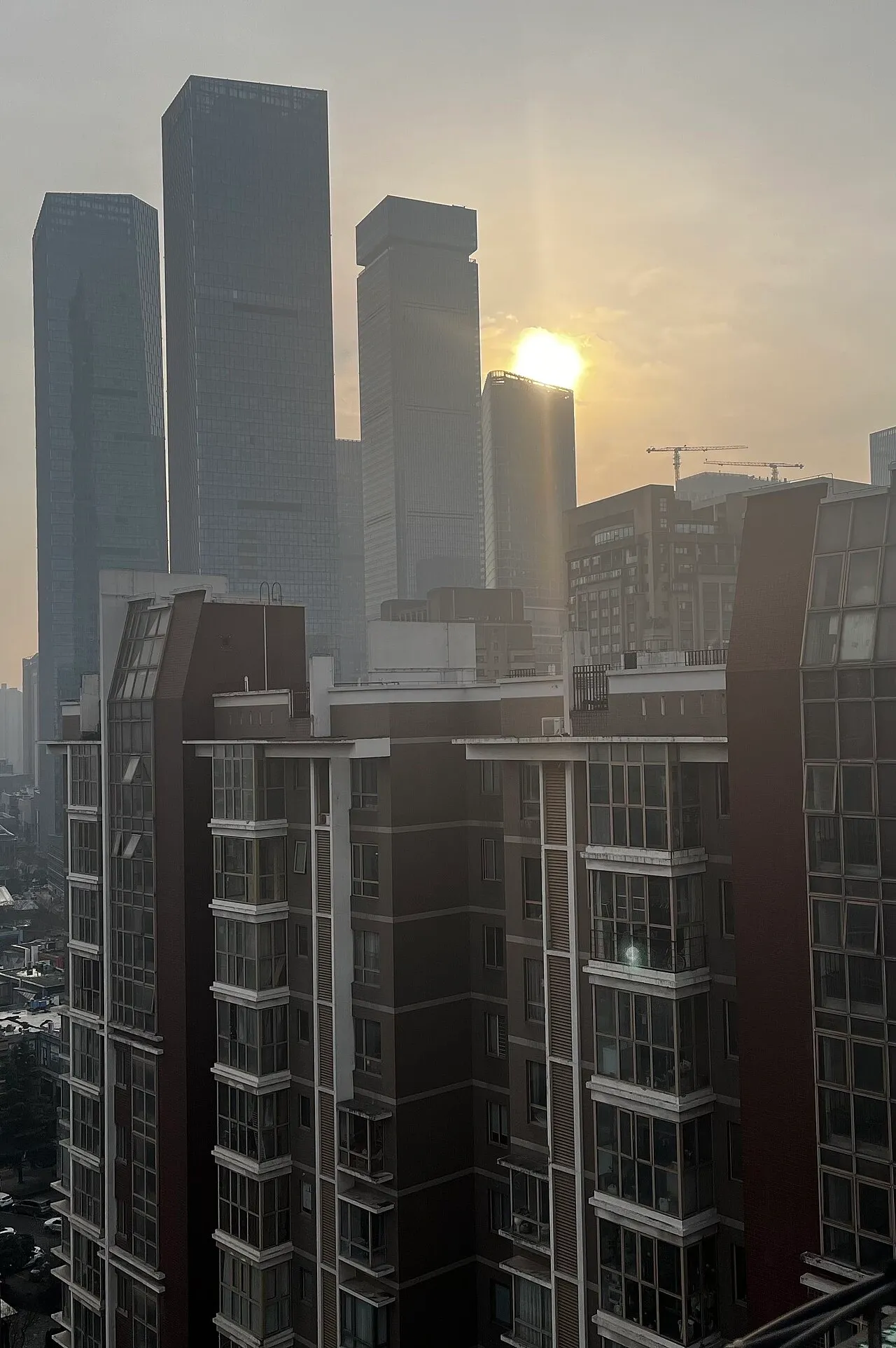 High-rise towers in morning backlight behind residential buildings.