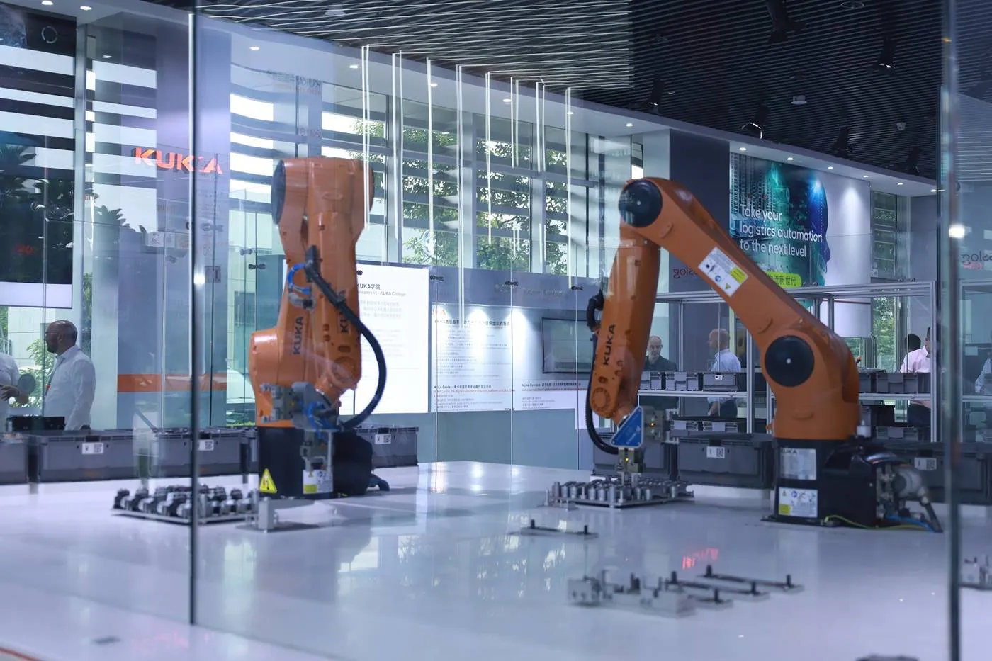 Two orange industrial robots behind a glass enclosure.