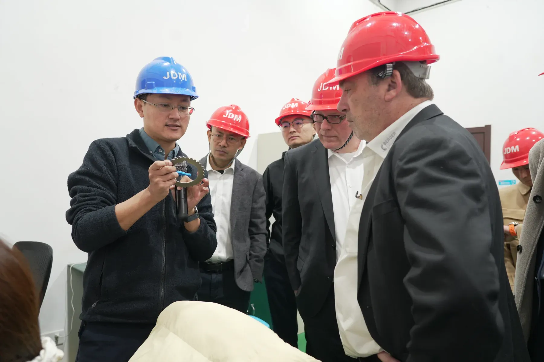 Ein Ingenieur erläutert deutschen Fachbesuchern ein bearbeitetes Bauteil