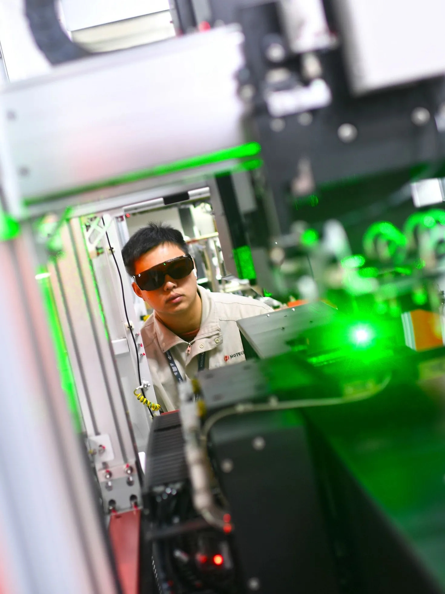 A technician wearing protective glasses beside laser-marking equipment with green light.